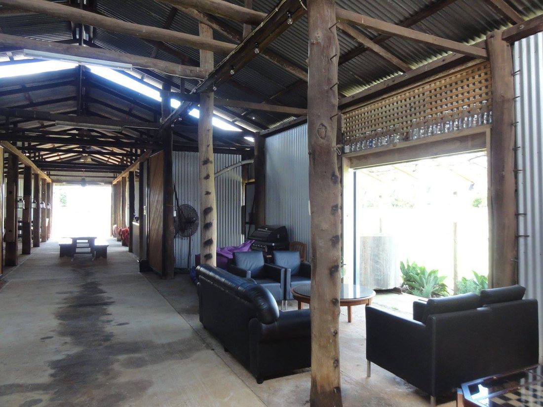 The quieter back section of the shed with a games table, cane bench and armchairs against the corrugated iron wall.