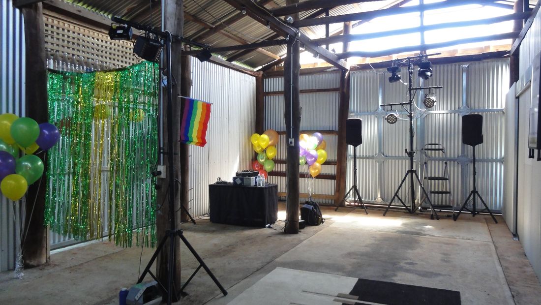 DJ and dance floor lighting rig set up inside the shed with speakers, balloons and a decorated backdrop ready for a function.