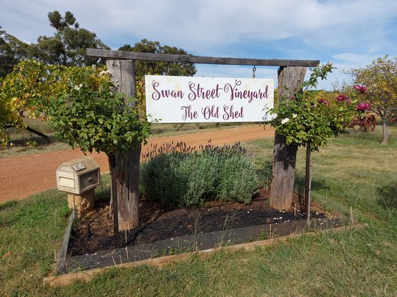 The Swan Street Vineyard entrance sign hung between two timber posts, surrounded by roses and lavender.