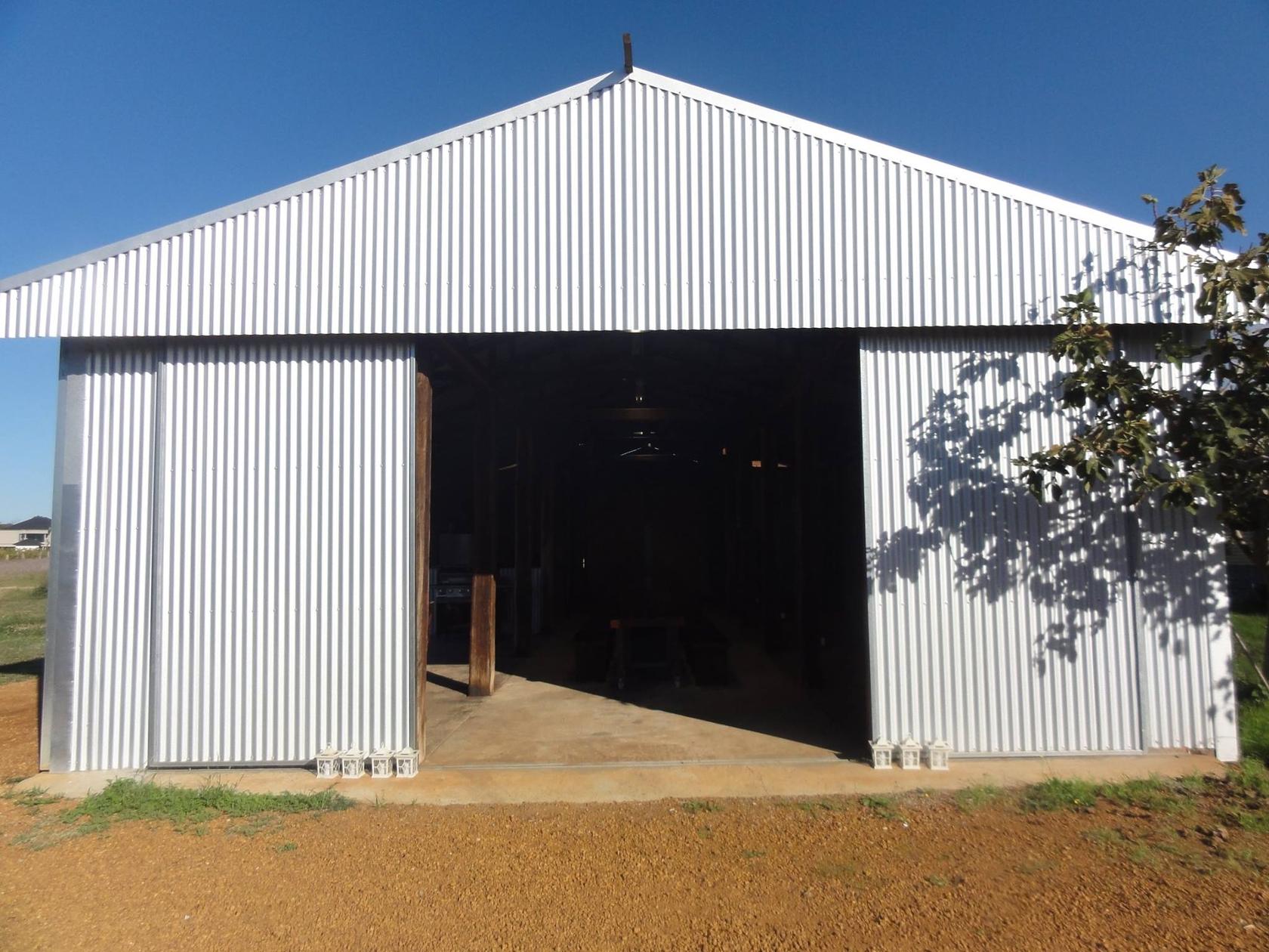 The Old Shed viewed from outside on a clear day, wide sliding doors open onto the concrete apron, with a fig tree beside the entrance.