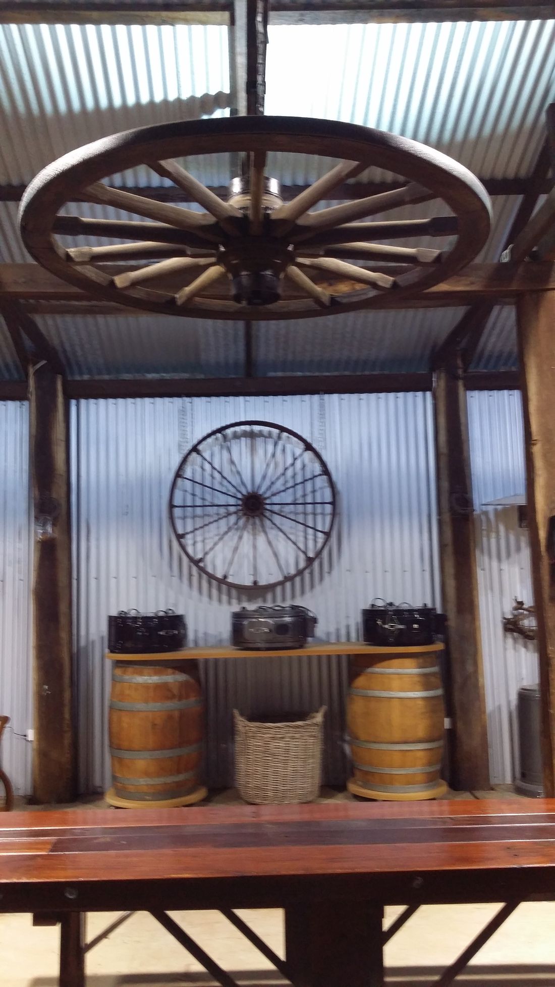 A restored wooden wagon wheel repurposed as a hanging light fitting above the bar area, with wine barrels and a second wheel mounted on the wall behind.